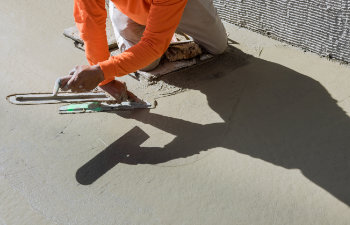 worker plasters wet cement concrete floor using trowel after pouring concrete in floor